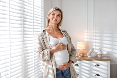 Portrait of beautiful pregnant woman near window at home