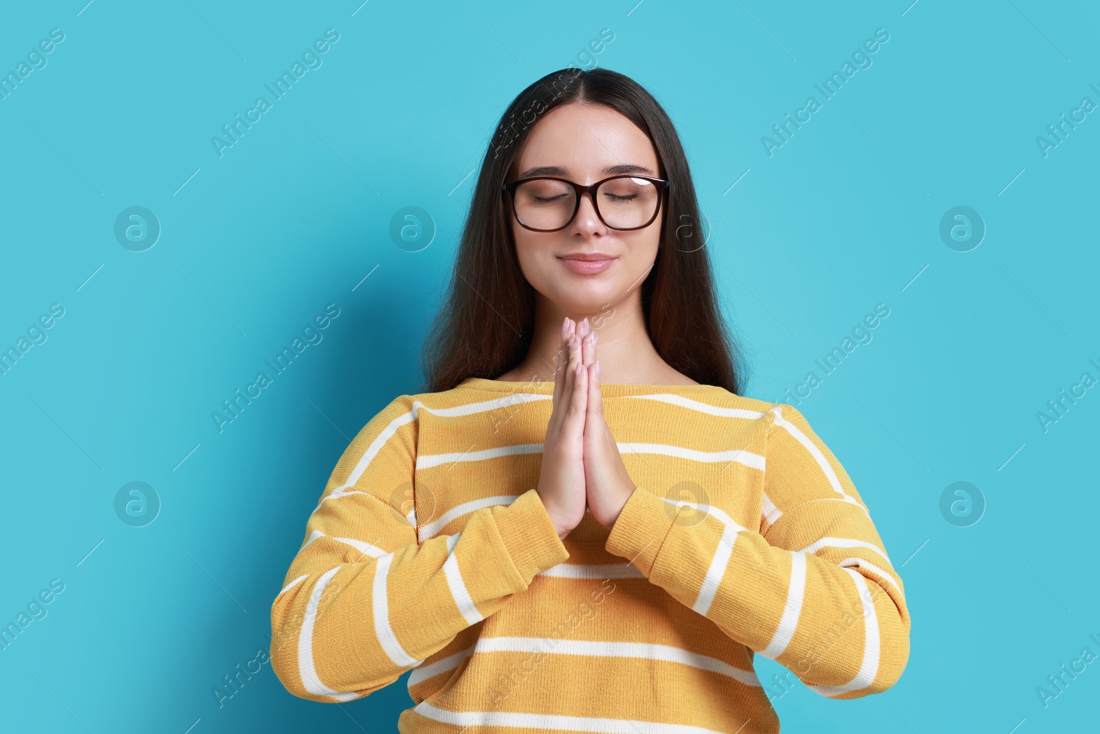 Photo of Young student praying for good exam result on light blue background