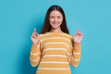 Photo of Excited young student crossing fingers on light blue background. Hope for good exam result