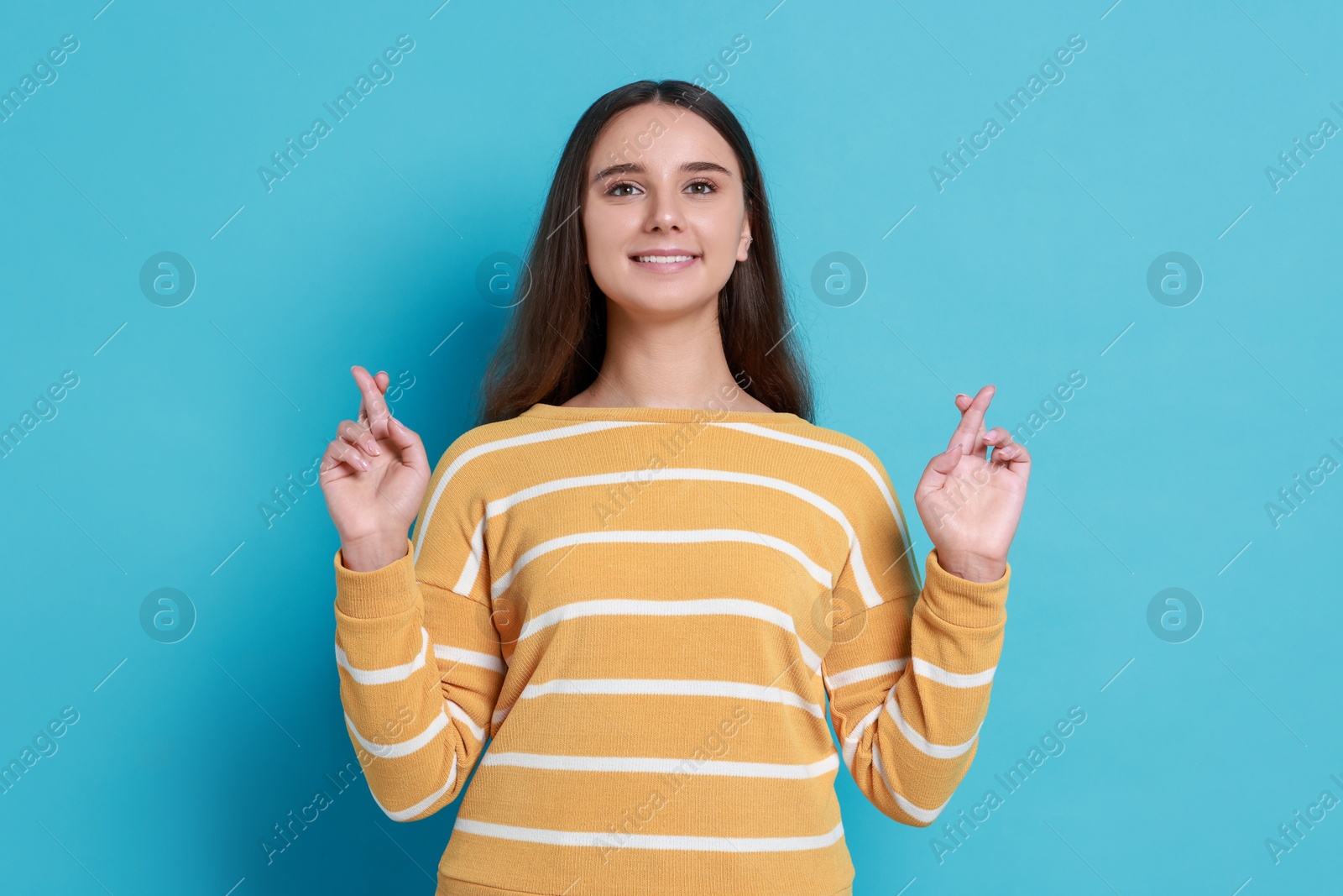 Photo of Excited young student crossing fingers on light blue background. Hope for good exam result