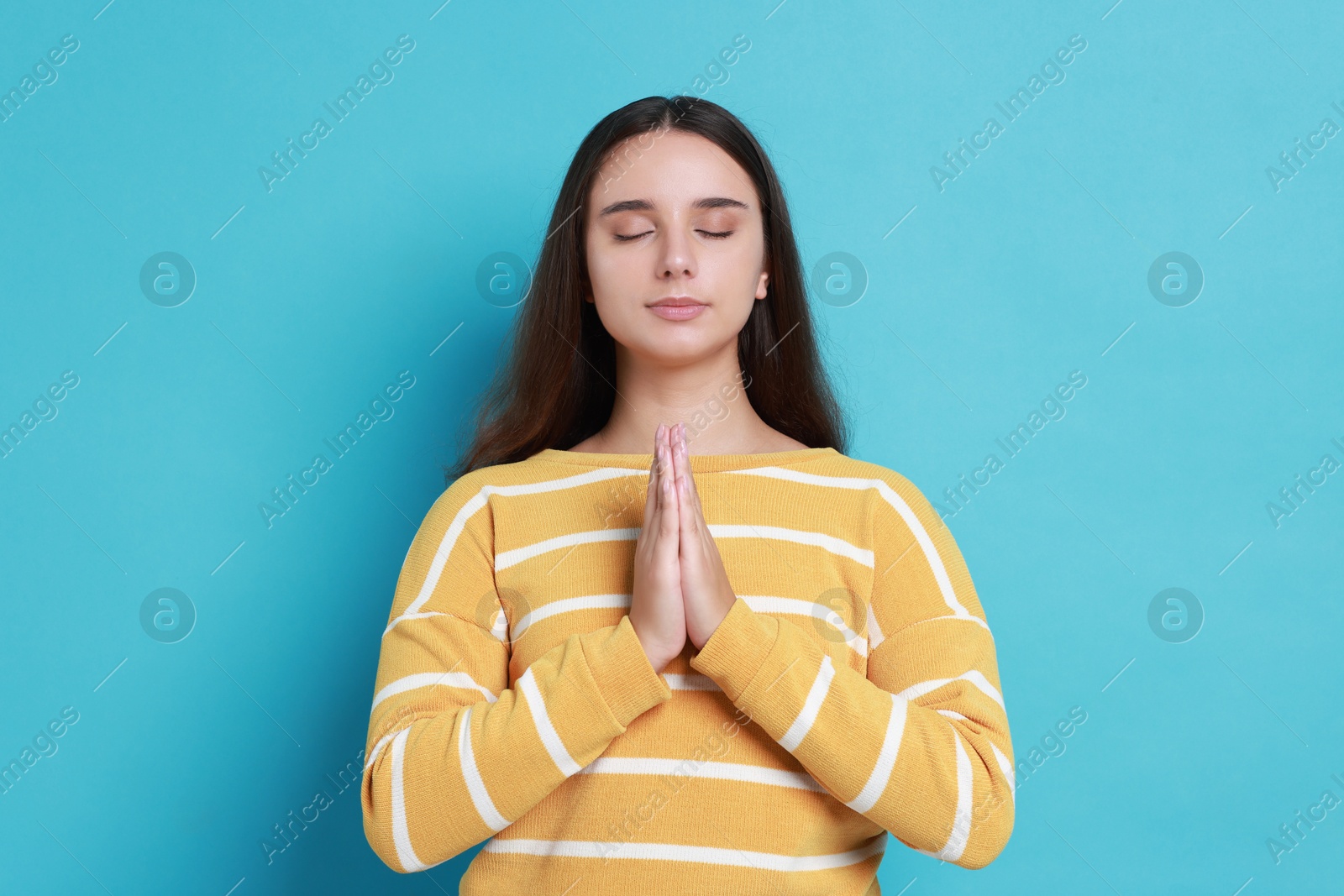 Photo of Young student praying for good exam result on light blue background