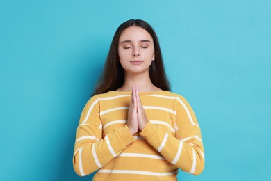 Photo of Young student praying for good exam result on light blue background