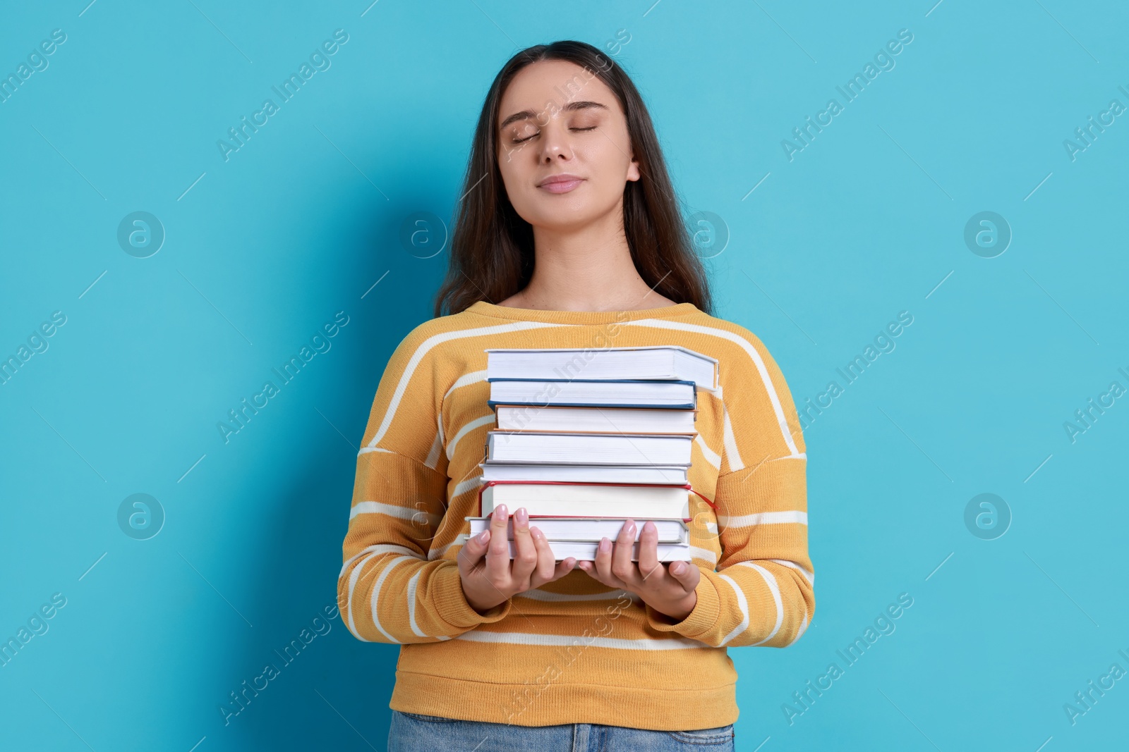 Photo of Young student with stack of books on light blue background