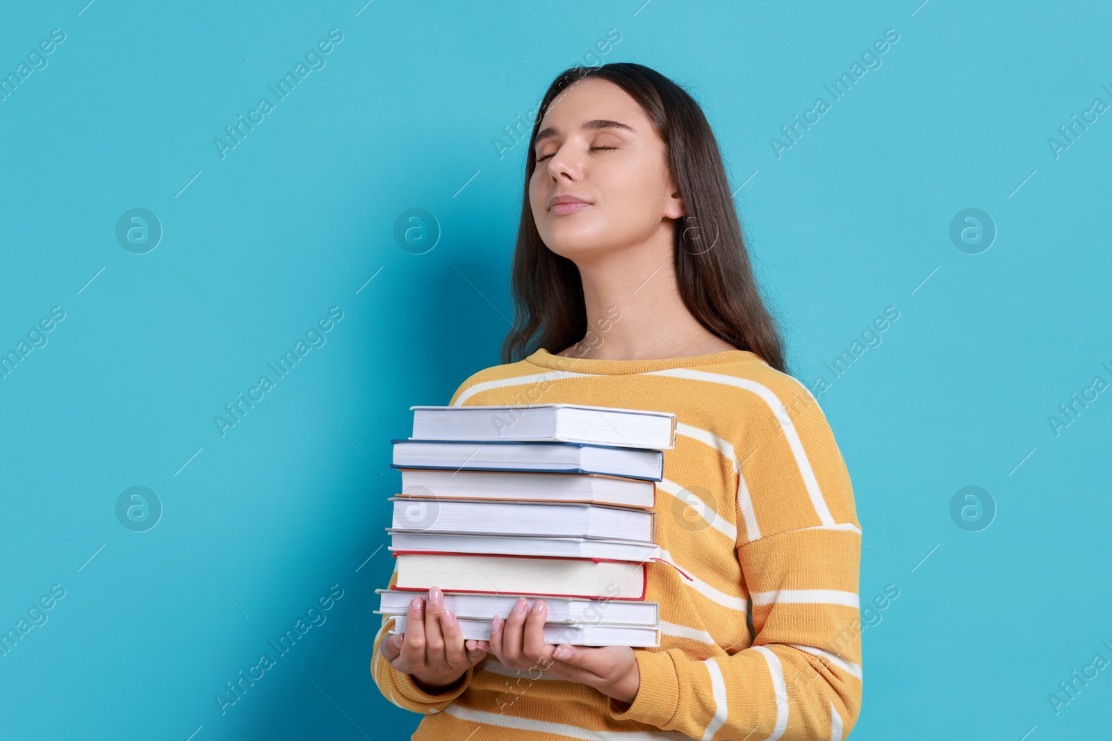 Photo of Young student with stack of books on light blue background