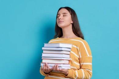 Young student with stack of books on light blue background