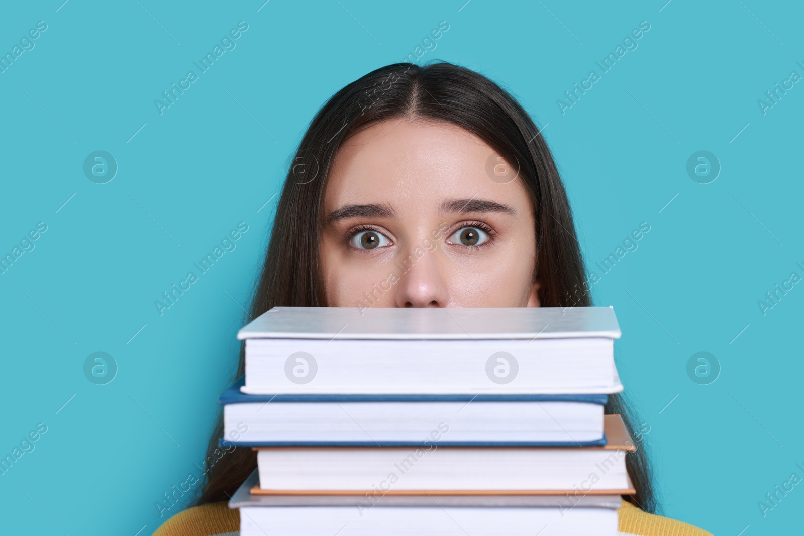 Photo of Young student with stack of books having stress before exam on light blue background, closeup