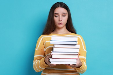 Photo of Young student with stack of books having stress before exam on light blue background