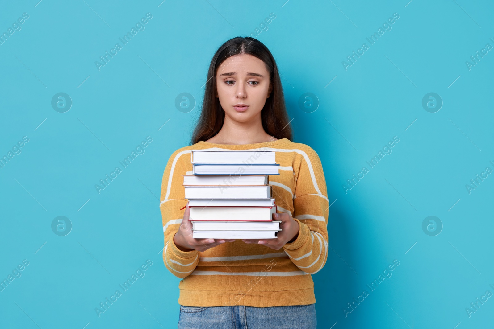 Photo of Young student with stack of books having stress before exam on light blue background