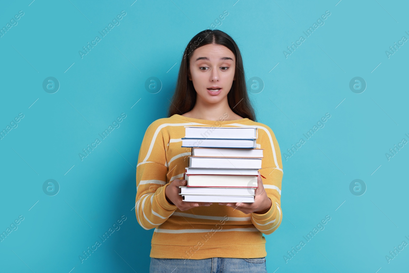 Photo of Young student with stack of books having stress before exam on light blue background