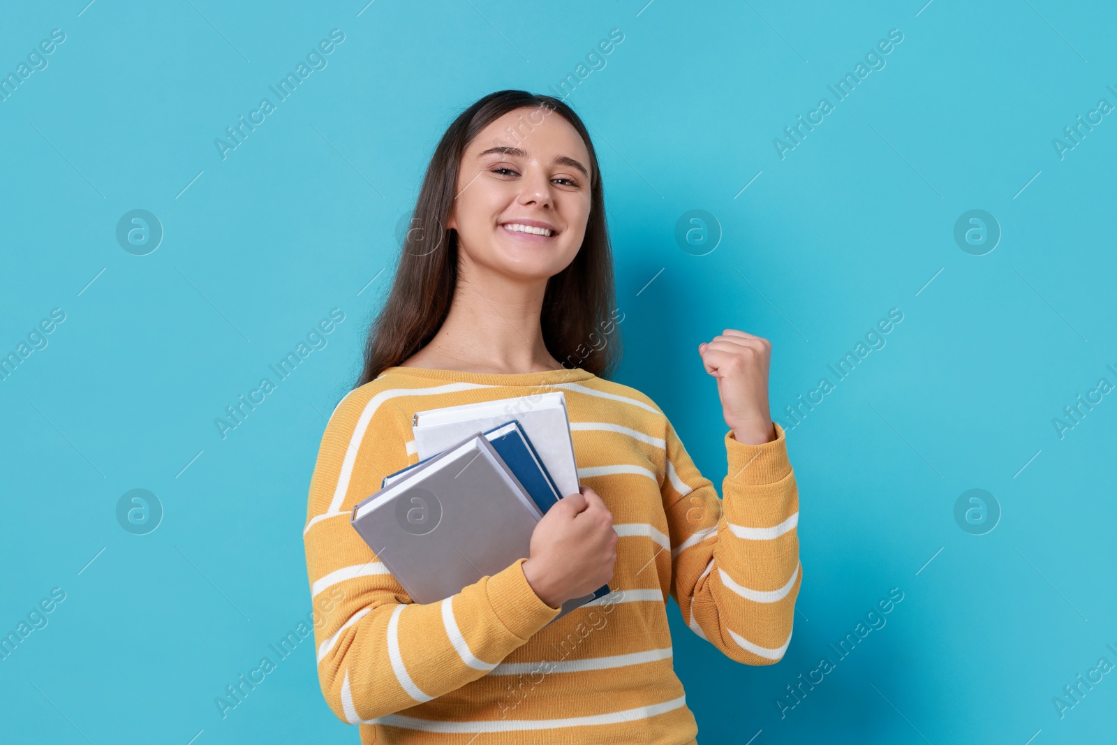 Photo of Young student with books happy about her good exam result on light blue background