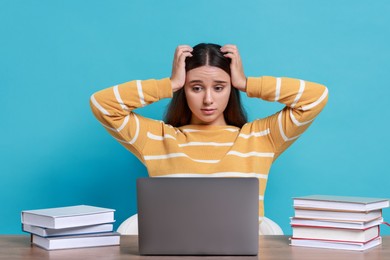 Photo of Young student with books and laptop having stress before exam at table against light blue background