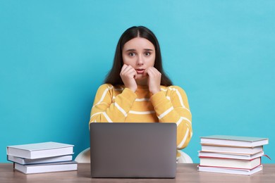 Photo of Young student with books and laptop having stress before exam at table against light blue background