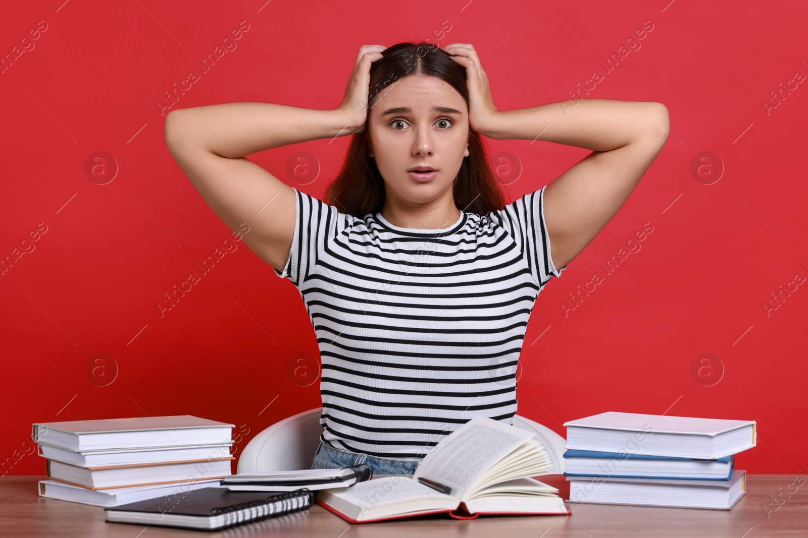 Photo of Young student having stress before exam at desk against red background