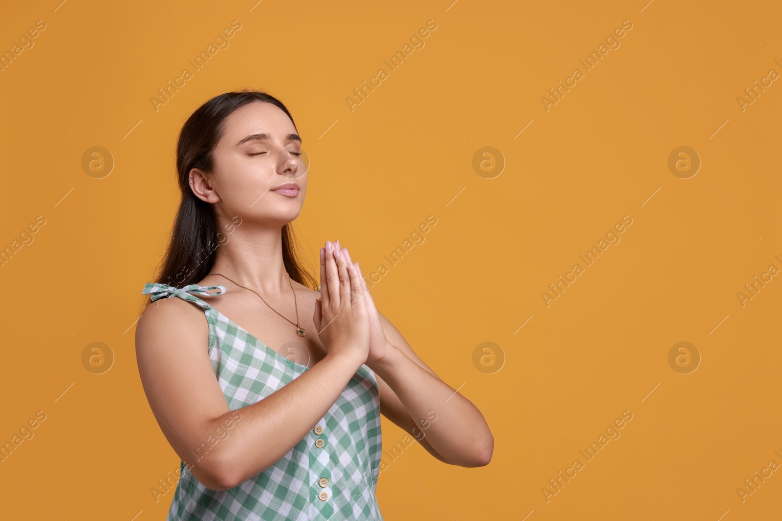 Photo of Young student praying for good exam result on orange background, space for text