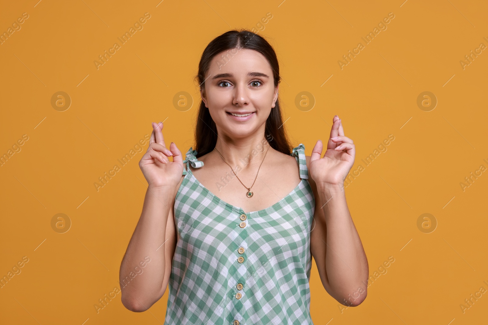 Photo of Excited young student crossing fingers on orange background. Hope for good exam result