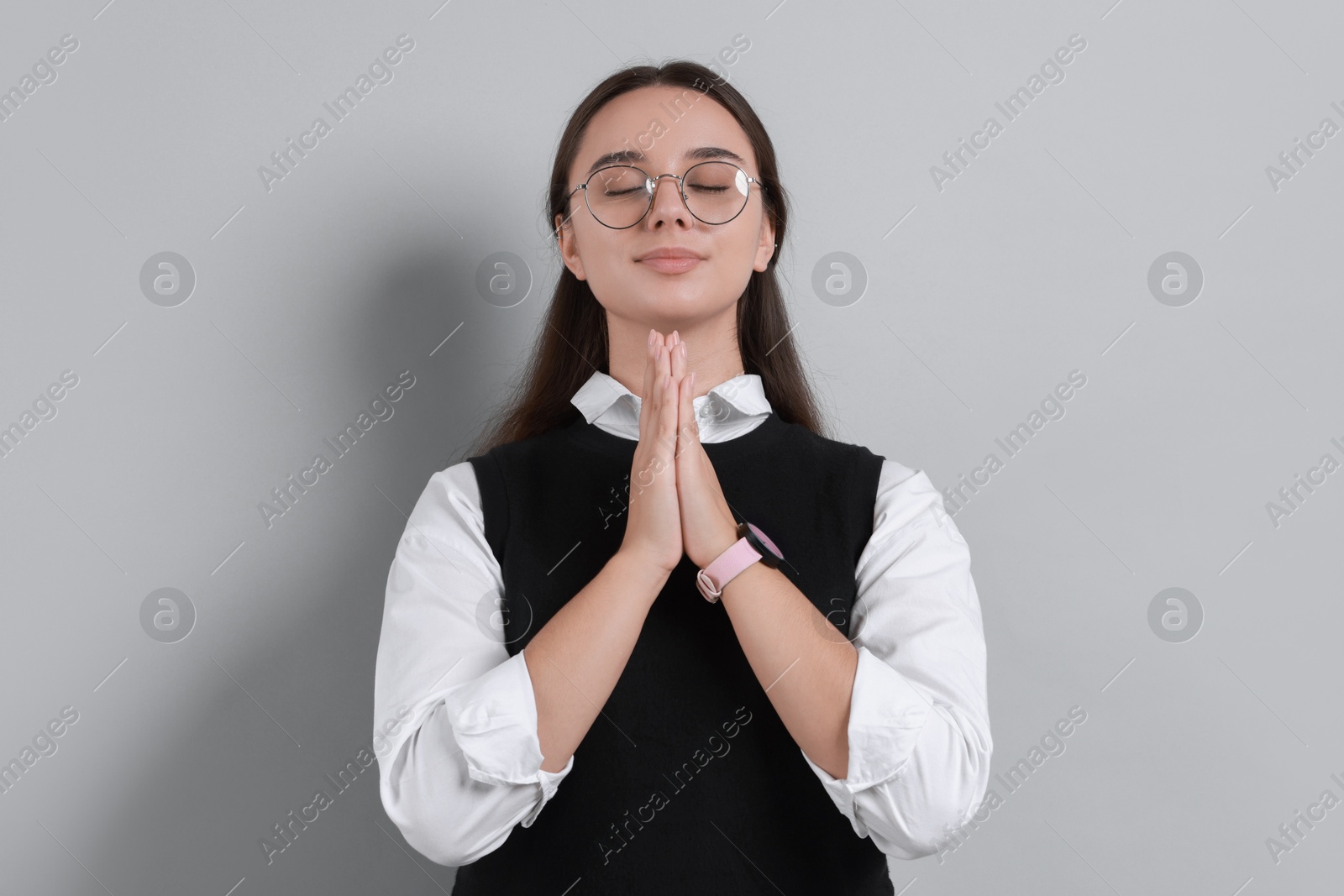 Photo of Young student praying for good exam result on grey background