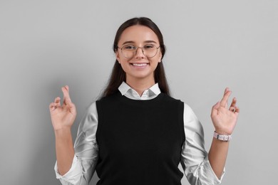 Photo of Excited young student crossing fingers on grey background. Hope for good exam result