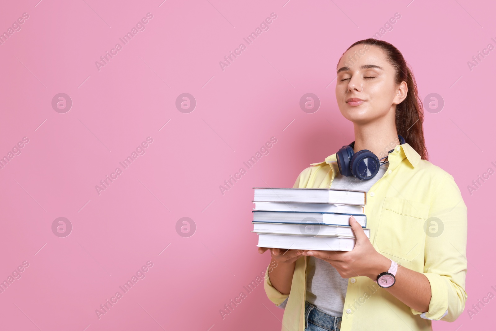 Photo of Young student with stack of books on pink background, space for text