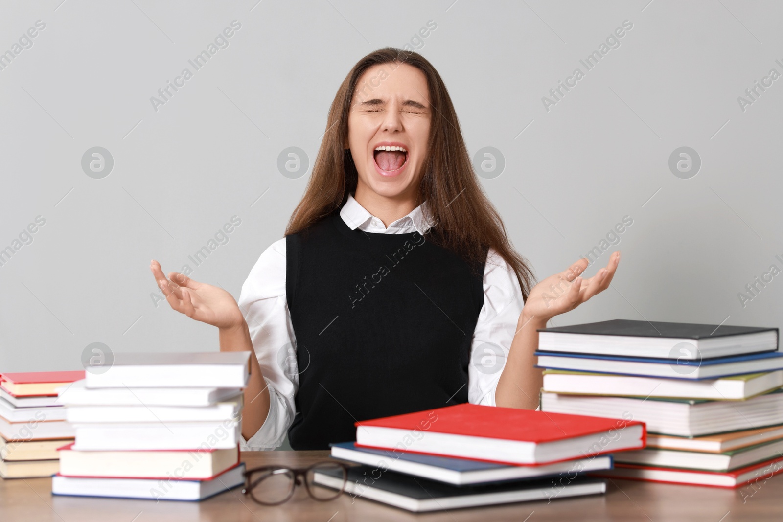 Photo of Emotional student having stress before exam at desk against grey background