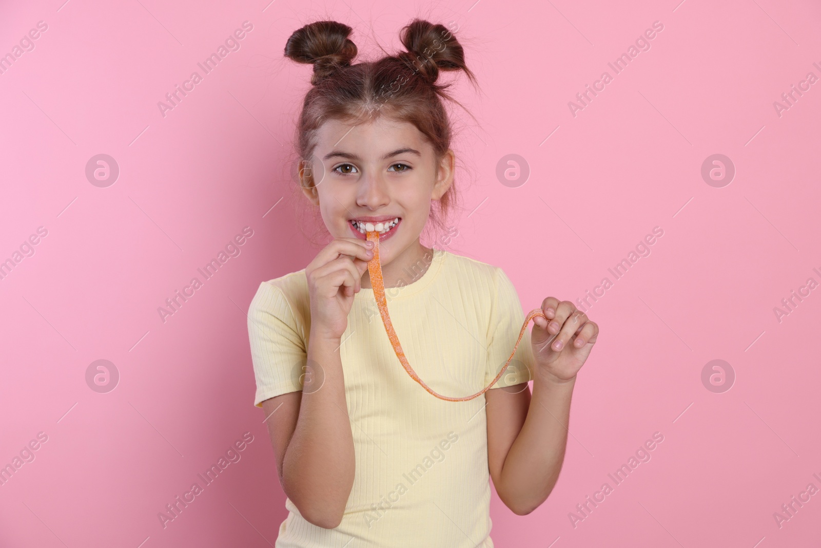 Photo of Happy girl eating tasty gummy candy on pink background