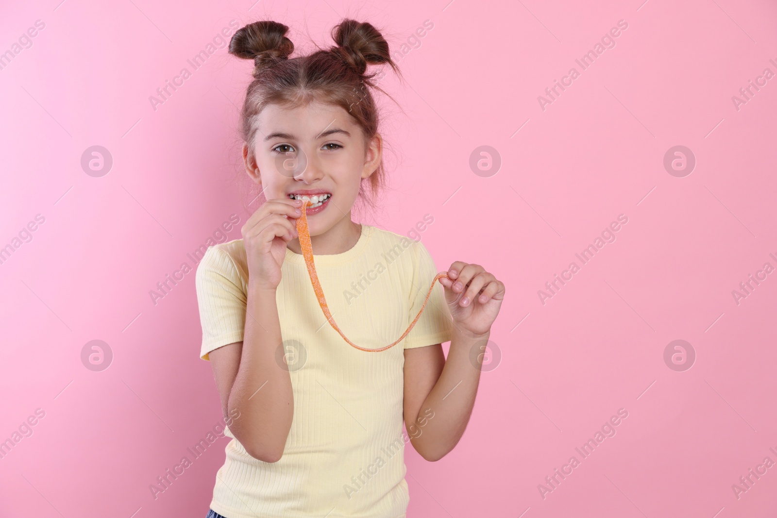 Photo of Happy girl eating tasty gummy candy on pink background. Space for text