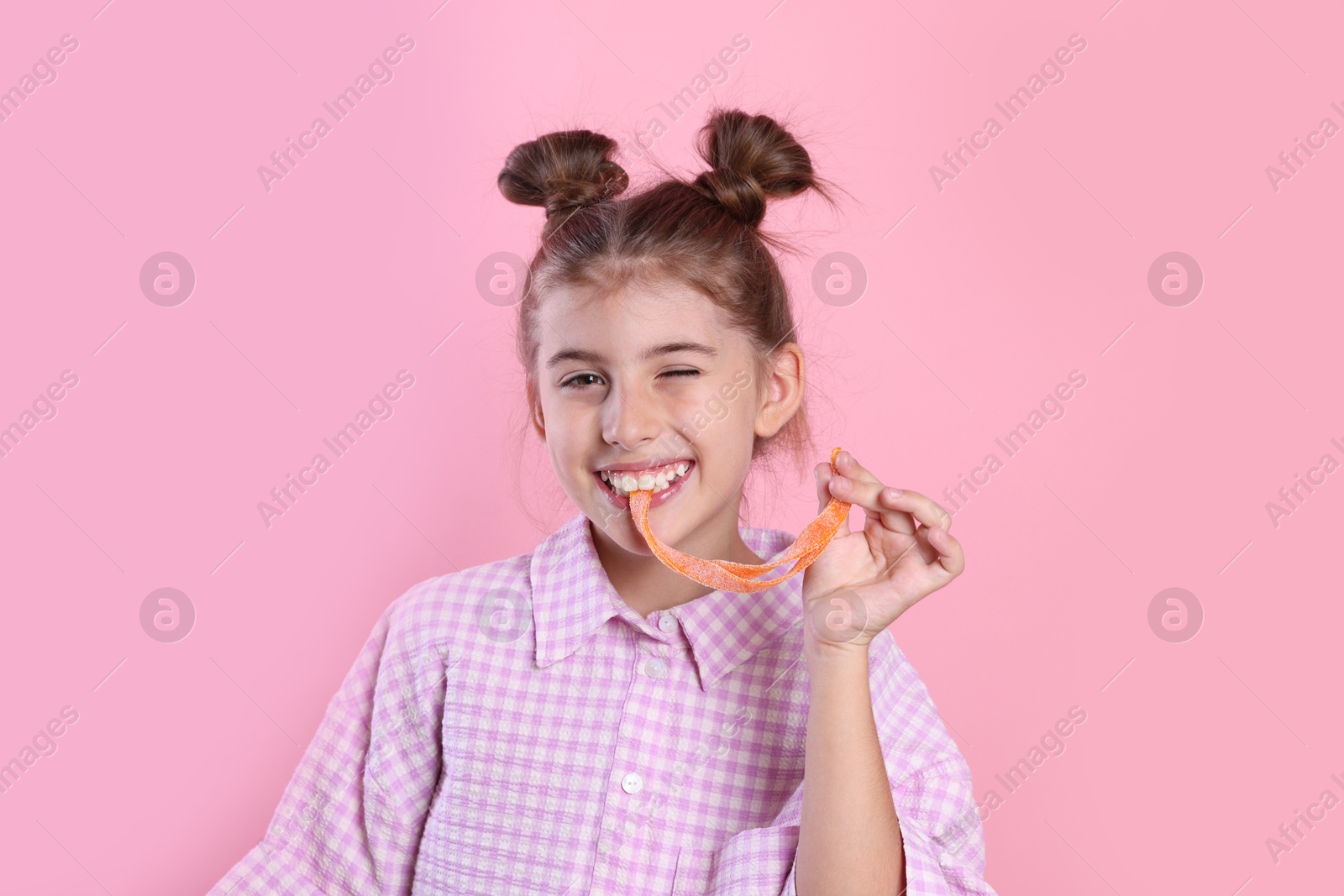 Photo of Happy girl eating tasty gummy candy on pink background