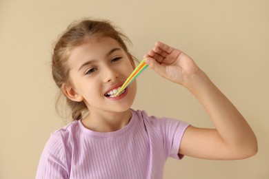 Photo of Little girl eating tasty rainbow sour belt on beige background