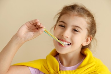 Happy girl eating tasty rainbow sour belt on beige background