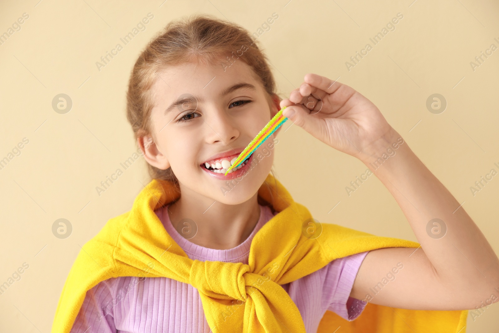 Photo of Happy girl eating tasty rainbow sour belt on beige background