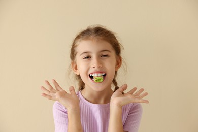 Photo of Happy girl eating tasty rainbow sour belt on beige background