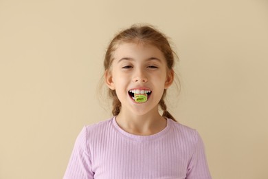 Photo of Happy girl eating tasty rainbow sour belt on beige background