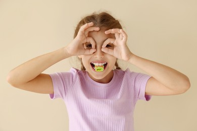 Photo of Happy girl eating tasty rainbow sour belt and gesturing on beige background