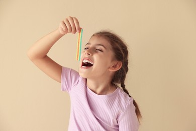 Little girl eating tasty rainbow sour belt on beige background