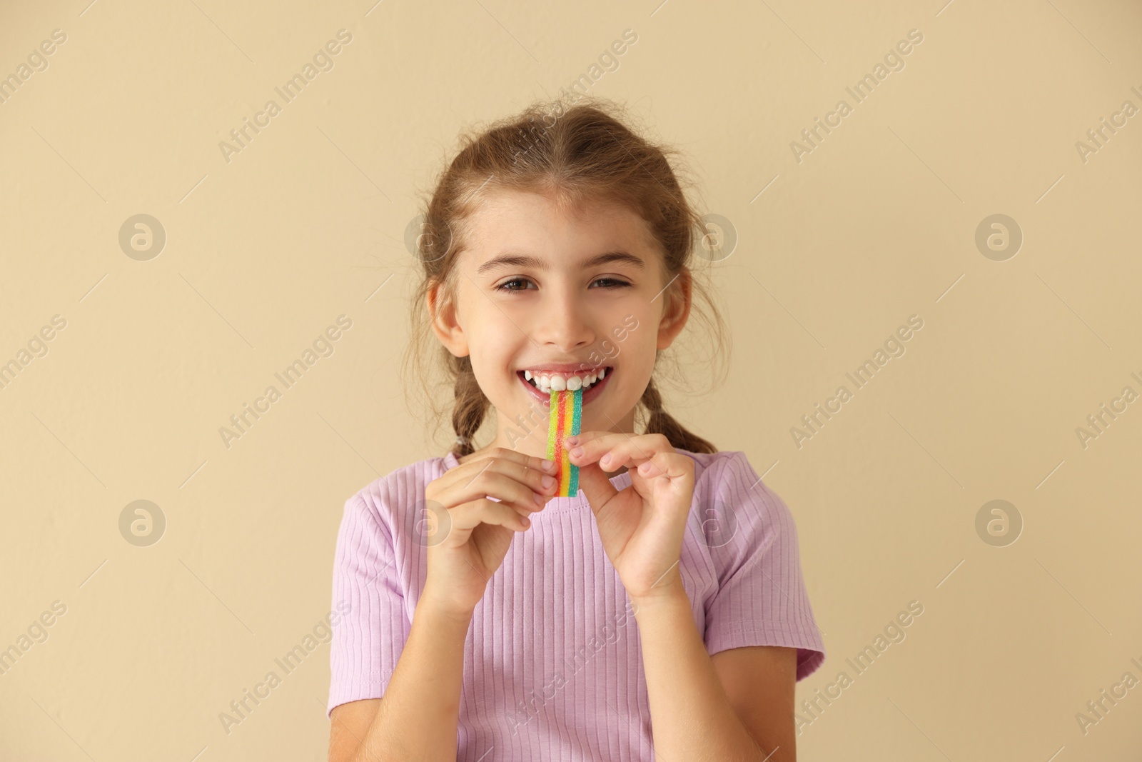 Photo of Happy girl eating tasty rainbow sour belt on beige background