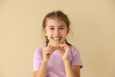 Photo of Happy girl eating tasty rainbow sour belt on beige background