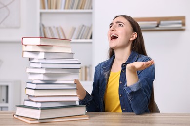 Photo of Excited student before exam screaming at table with stack of books indoors