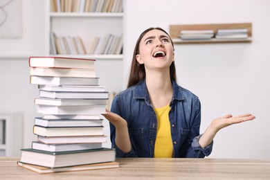 Photo of Excited student before exam screaming at table with stack of books indoors