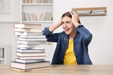 Photo of Excited student before exam screaming at table with stack of books indoors