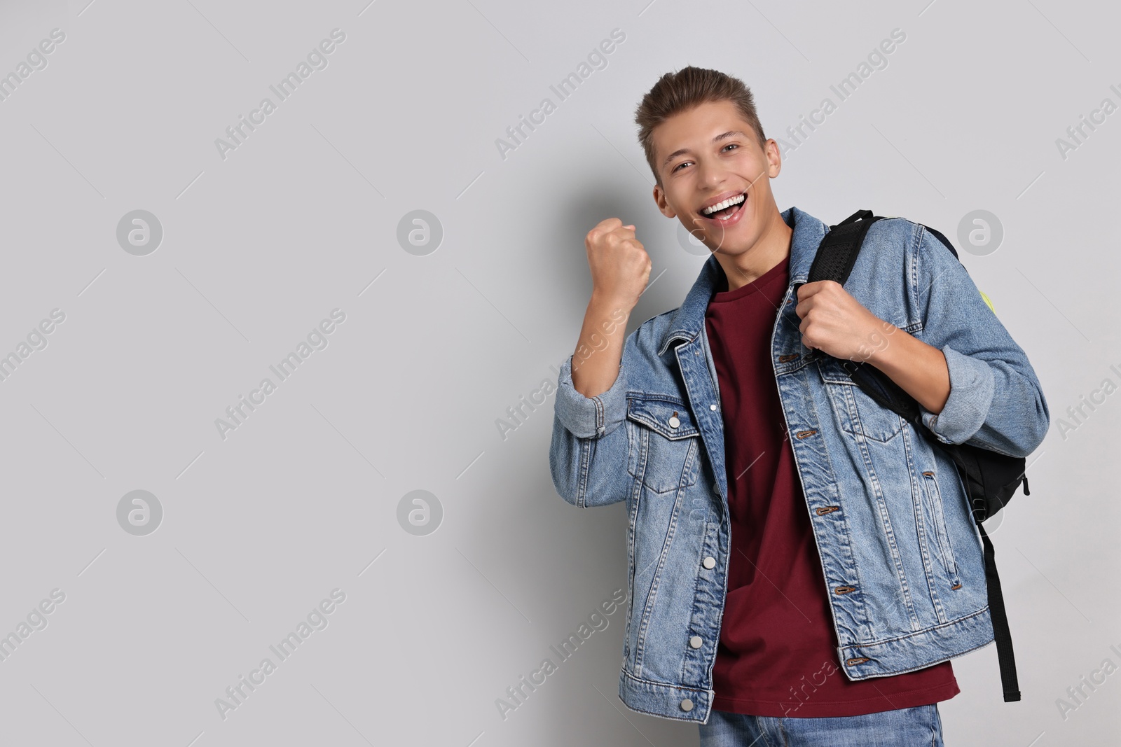 Photo of Student with backpack feeling happy about his good exam result on grey background. Space for text