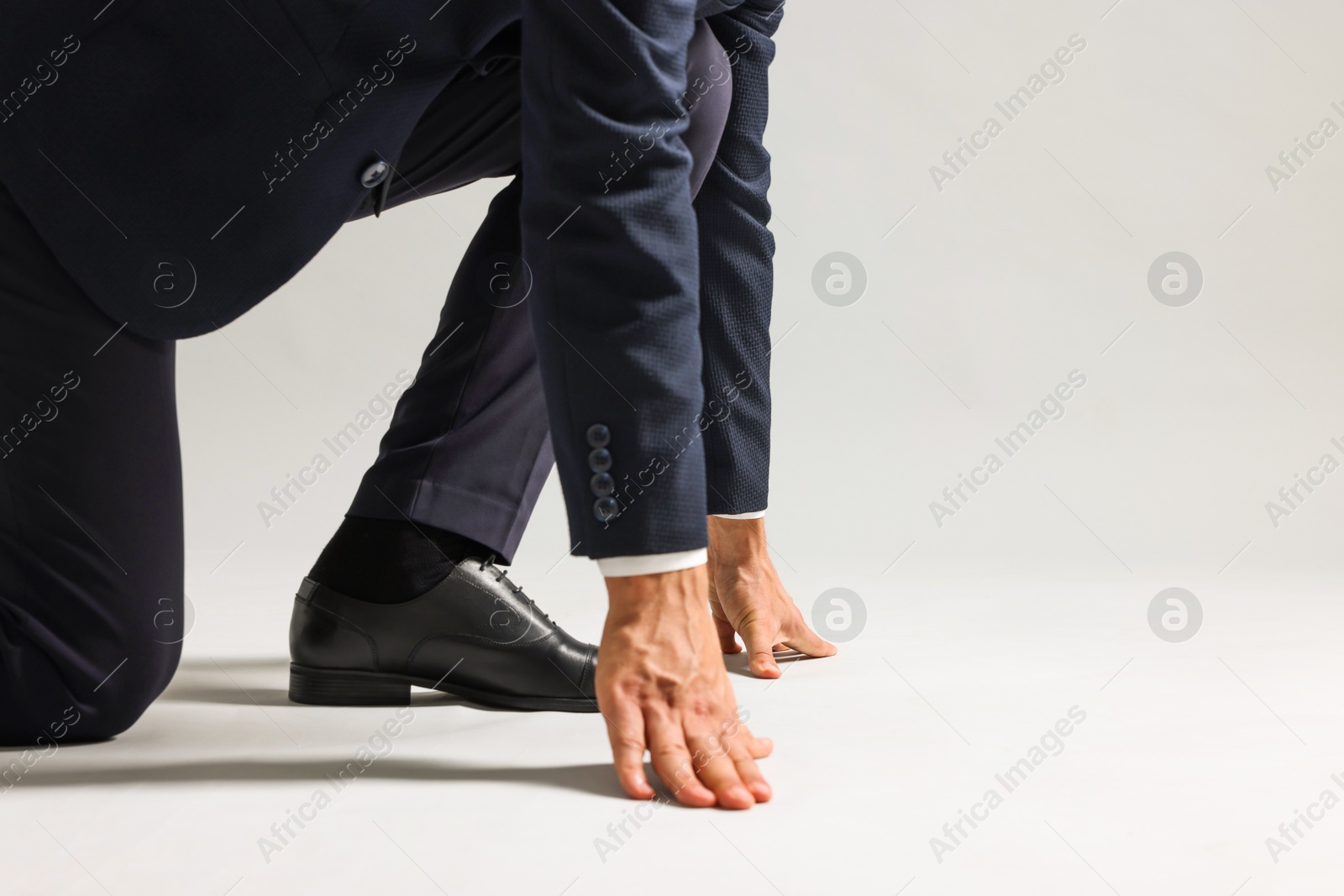 Photo of Businessman in starting position for run on light grey background, closeup. Space for text