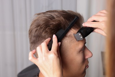 Photo of Professional barber making stylish haircut in salon, closeup