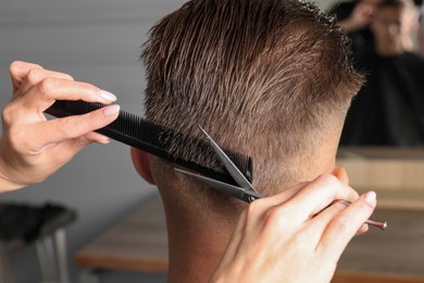 Photo of Professional hairdresser cutting client's hair with scissors in barbershop, closeup