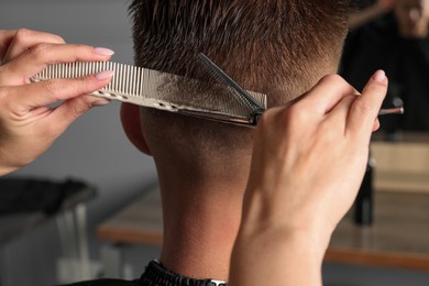 Photo of Professional hairdresser cutting client's hair with scissors in barbershop, closeup