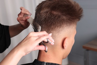 Photo of Professional hairdresser cutting client's hair with scissors in barbershop, closeup