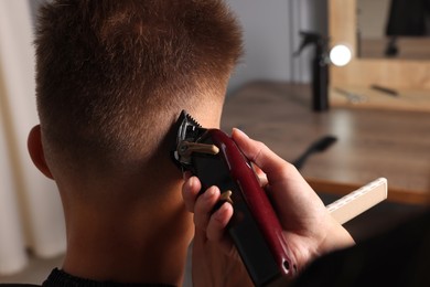 Photo of Professional barber making stylish haircut in salon, closeup