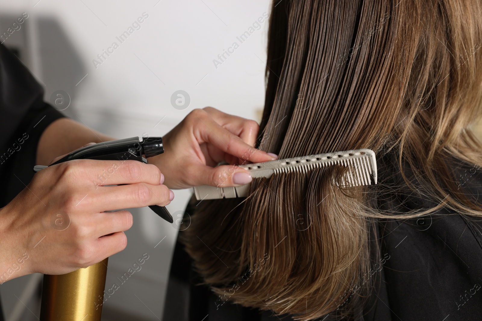 Photo of Hairdresser using spray while making stylish haircut in salon, closeup