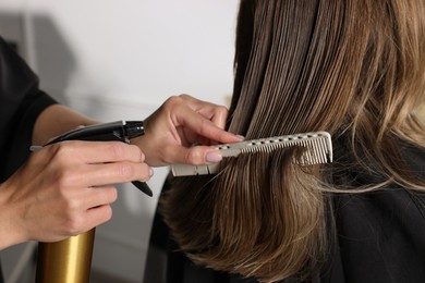 Hairdresser using spray while making stylish haircut in salon, closeup