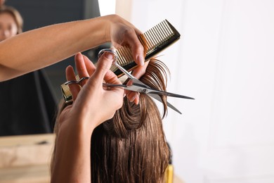 Photo of Hairdresser cutting client's hair with scissors in salon, closeup