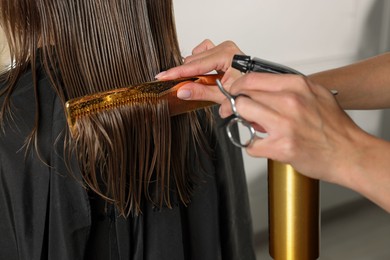 Photo of Hairdresser using spray while making stylish haircut in salon, closeup