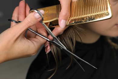 Photo of Hairdresser cutting client's hair with scissors in salon, closeup